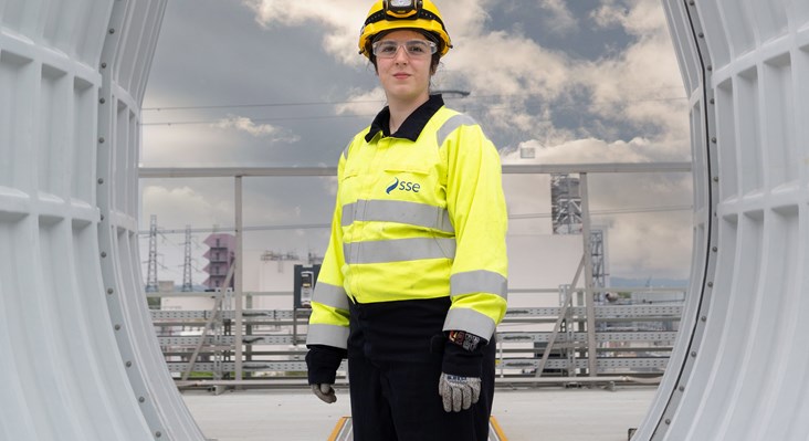 A young female engineer stood in the centre of power station infrastructure and smiling